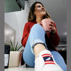 modelo sosteniendo una taza de café sin nombre con tenis blancos y maceta de fondo